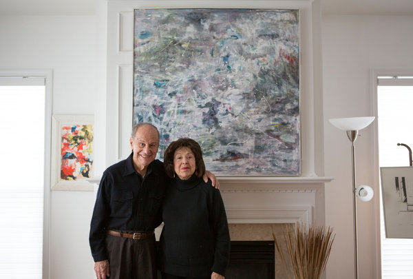 The painter Nelly Toll, a Holocaust survivor, and her husband, Herb Toll, in front of two of her recent paintings in their home in Vorhees, N.J. Credit Jessica Kourkounis for The New York Times