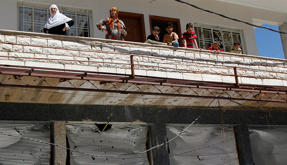 People look out from a balcony above shops with damaged shutter fronts in the Madaya area, near Damascus, May 6, 2012.  (photo by REUTERS/Khaled al-Hariri)
