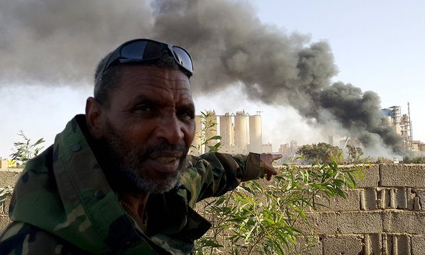 A fighter loyal to the eastern regime outside a Benghazi factory set ablaze in clashes on Friday. The civil war is raging amid efforts to form a single government. Photograph: Reuters