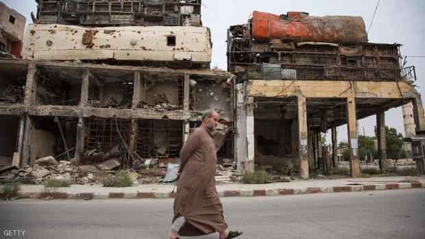 A Syrian man walks past a makeshift barricade made of the wreckage of buses to obstruct the view of regime snipers on May 2, 2016, in Aleppo's Bab al-Hadid neighbourhood which was targeted recently by government forces air strikes.  Aleppo residents ventured out onto the streets, taking advantage of a lull in violence in the northern Syrian city as the United States pushed to salvage a ceasefire. / AFP / KARAM AL-MASRI